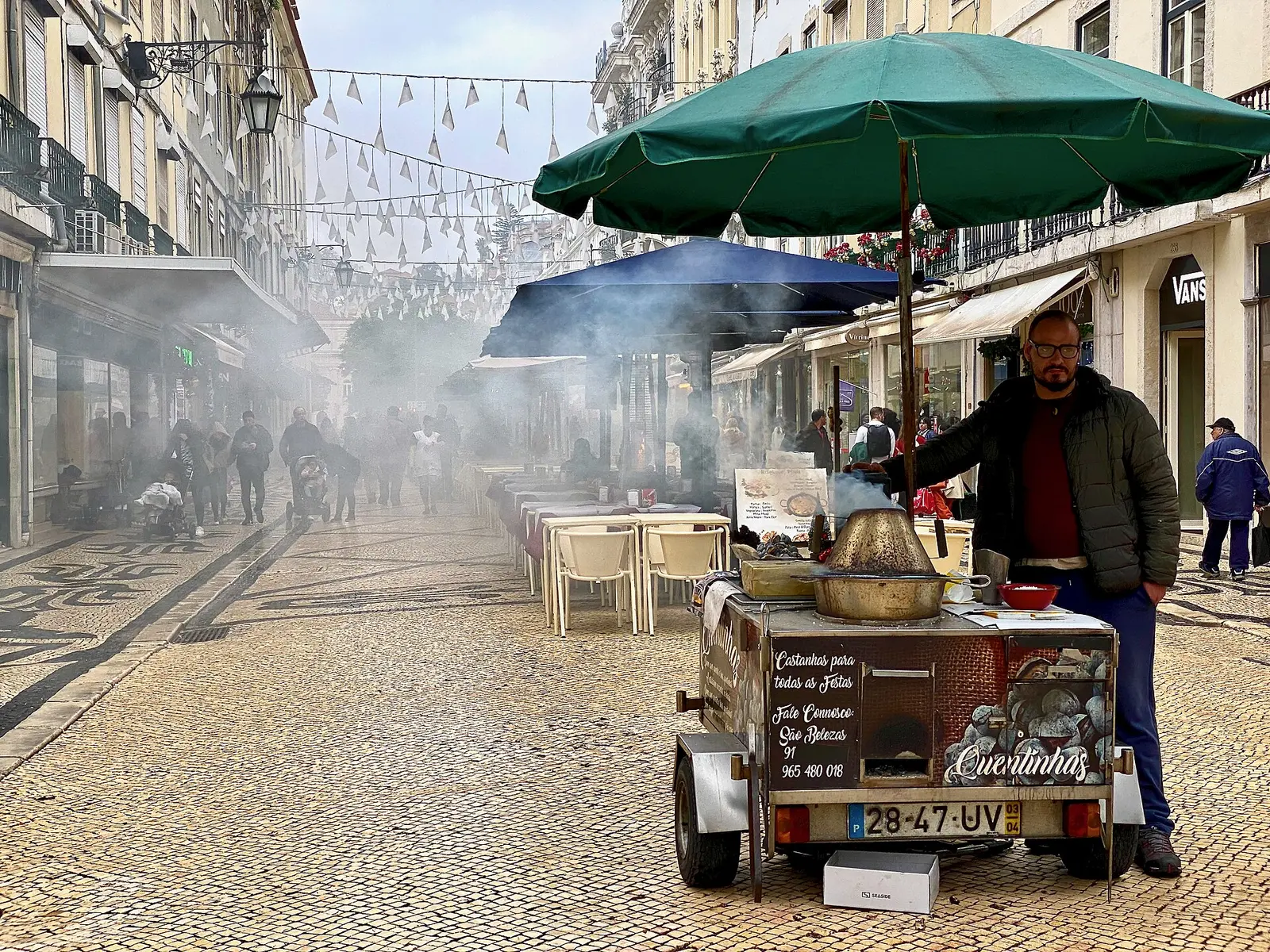 A roasted chestnut seller's cart filling a Baixa street with smoke