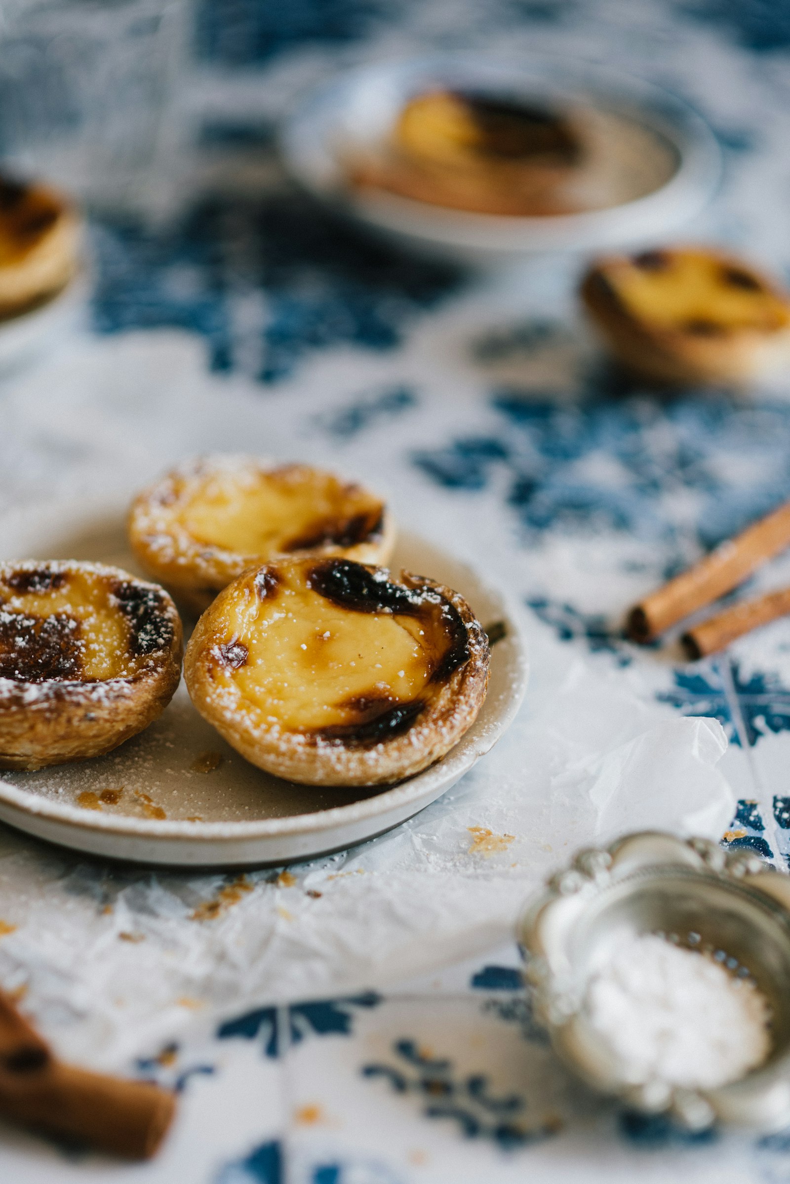 Pastéis de nata dusted with sugar on a plate over blue and white tiles
